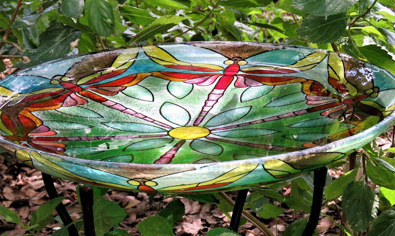 Glass mosaic bird bath sitting on steel legs among foliage