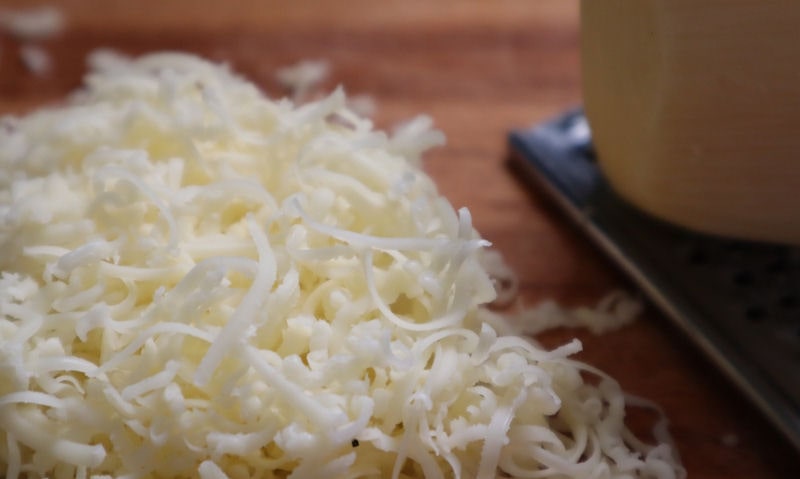 Freshly grated Gouda cheese, piled on chopping board next to grater