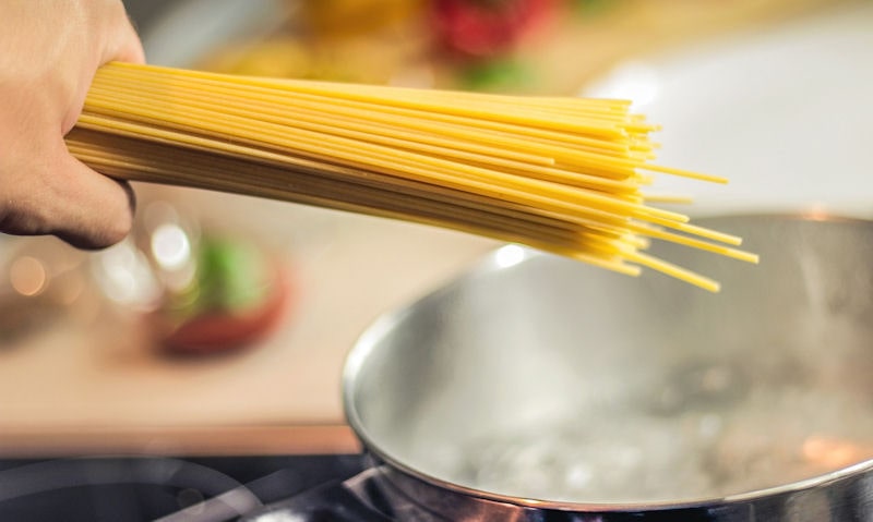 Person holding spaghetti style pasta over boiling pan of water on stove