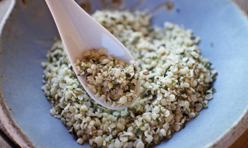 Spoonful of Hemp seed being shown to camera, Hemp seed in bowl below