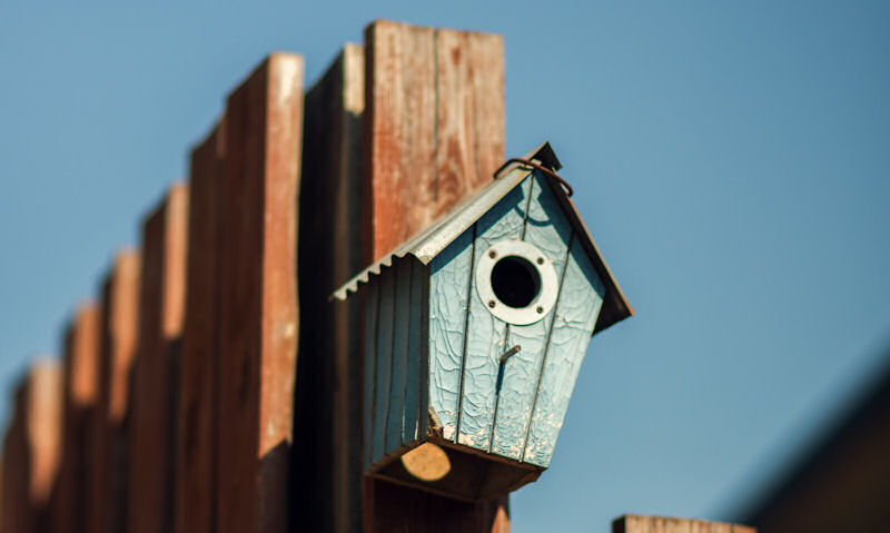 Blue birdhouse hung or mounted to fence post on the corner
