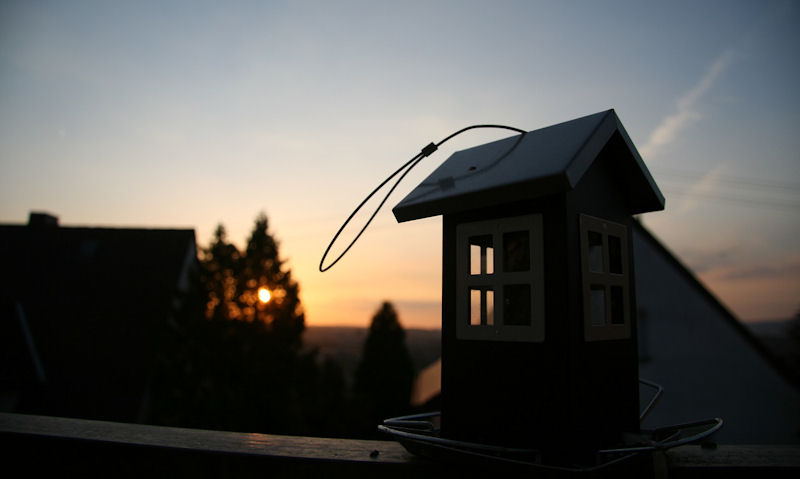 Bird seed feeder resting on porch railing at sunset