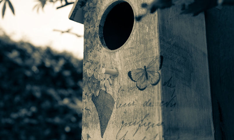 Weathered bird house decorated in finely printed works of art, in the shape of an accurate butterfly