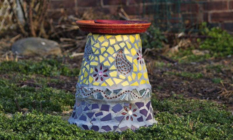 Short mosaic effect bird bath situated on lawn