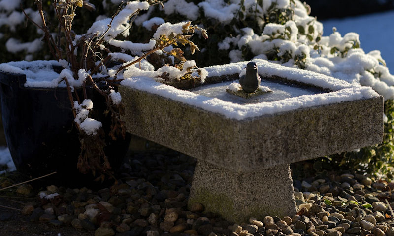 Iced up stone bird bath with snow coverage